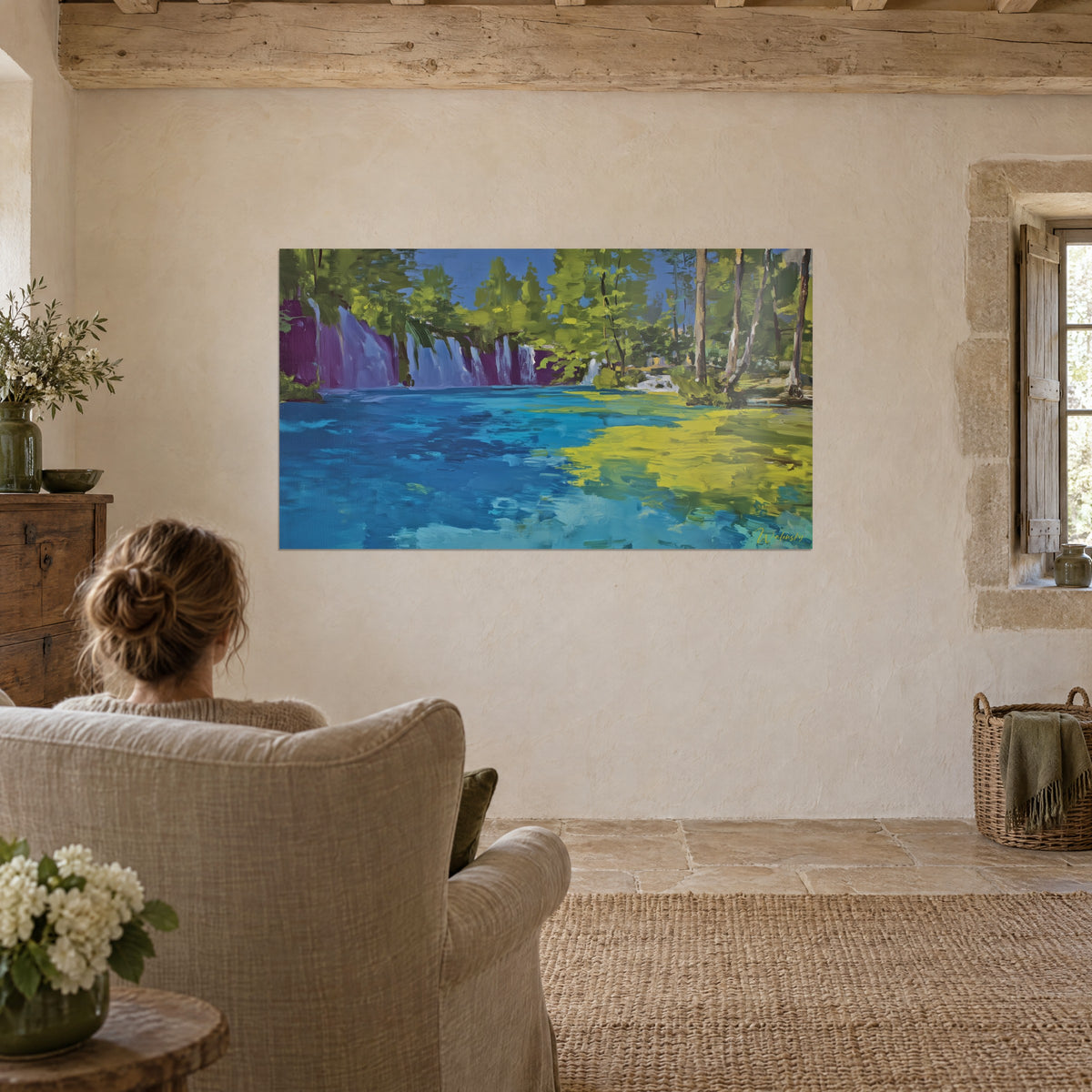 Cuadro agua cian veteada de amarillo, cascadas malva y sotobosque verde, mujer de espaldas en un sillón de lino frente a la pared de piedra