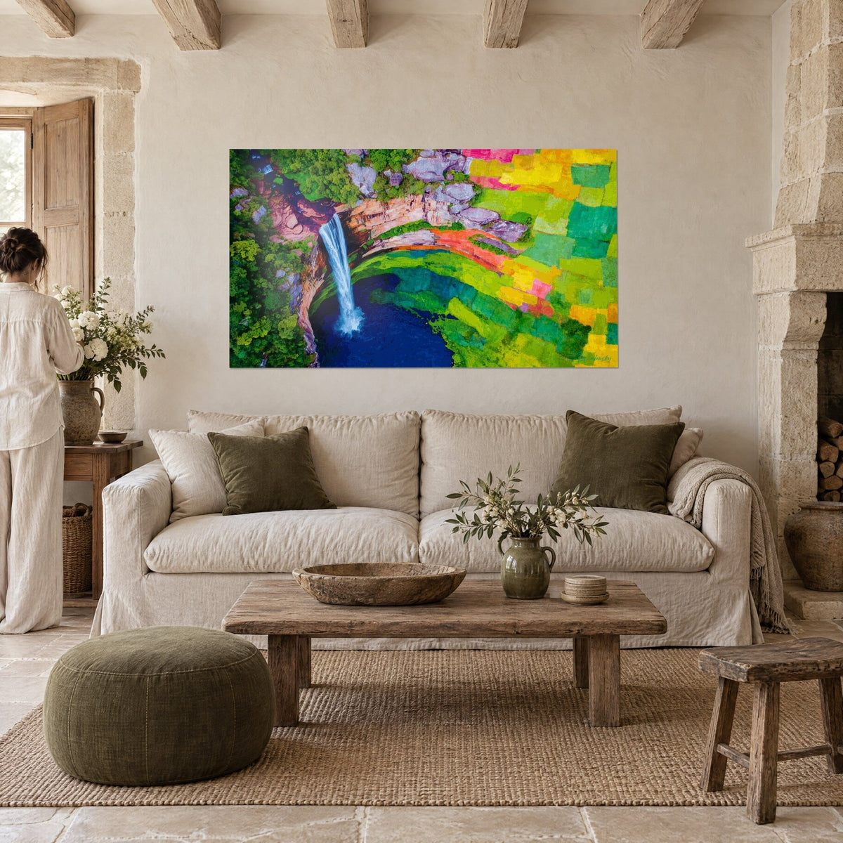 Wall art aerial view of a waterfall, white stream into a navy blue pool, yellow and green fields, above a sofa in a bright living room