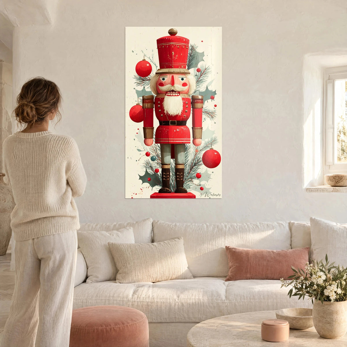 Quadro di un soldatino di legno rosso con baffi bianchi, palline scarlatte e agrifoglio verde salvia, sopra un divano in un soggiorno luminoso