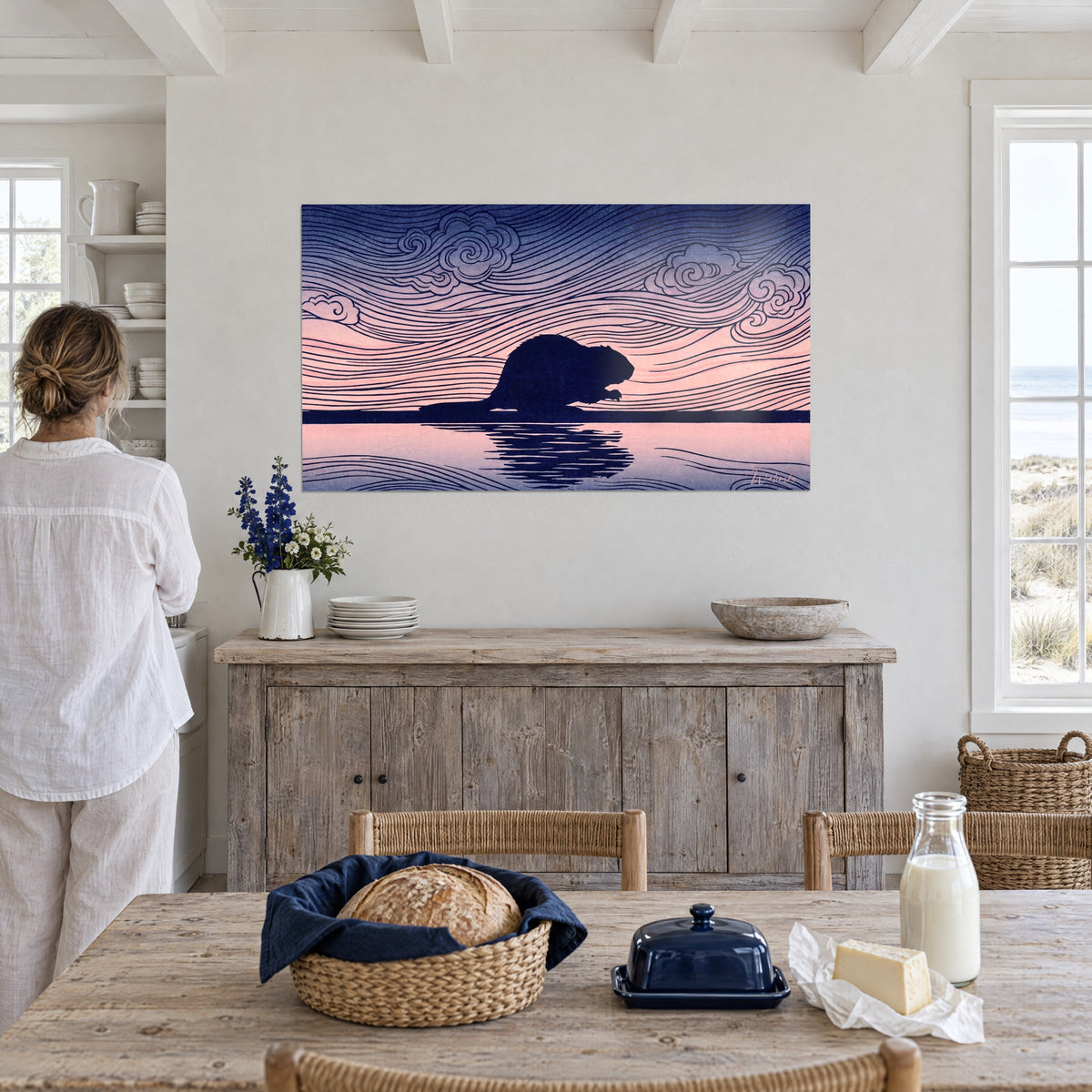 Schilderij bever in tegenlicht in indigo, zalmroze water dat zijn silhouet weerspiegelt, lucht met blauwe golven, boven een grijs dressoir in een huis aan zee