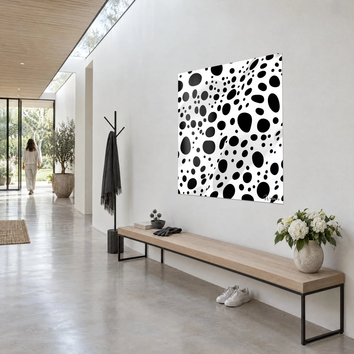 Quadro con pois neri di tutte le dimensioni e chiazze grigie su bianco, visto di scorcio accanto a una panca di legno e a un mazzo di fiori bianchi
