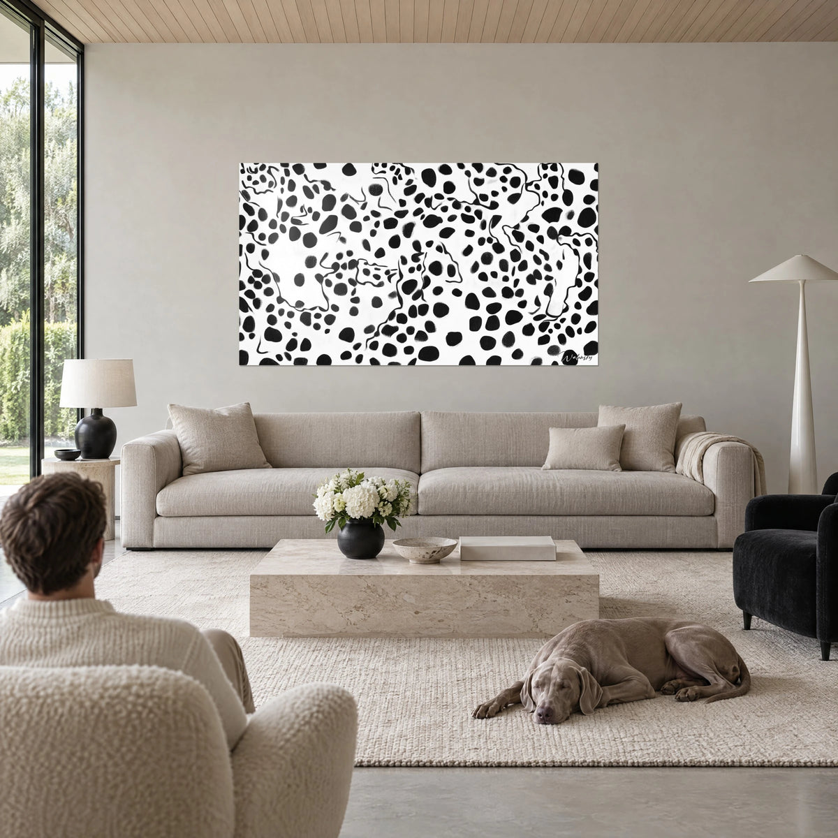 Gemälde mit schwarzem Leopardenfleckenmuster auf weißem Grund, zwei Personen und ein graues Hündchen, über einem Sofa in einem hellen Wohnzimmer