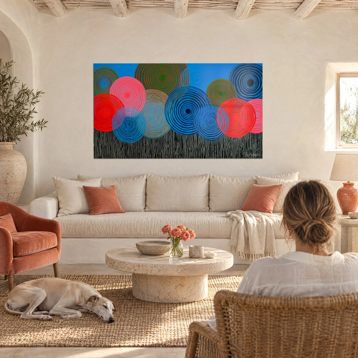 Cuadro con discos concéntricos rojos y azules sobre un fondo de líneas blancas, encima de un sofá en un salón luminoso