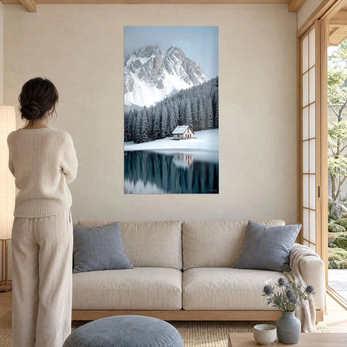 Tableau chalet blanc au pied d'une paroi rocheuse enneigée, sapins gris-vert et lac sombre, au-dessus d'un canapé dans un salon lumineux