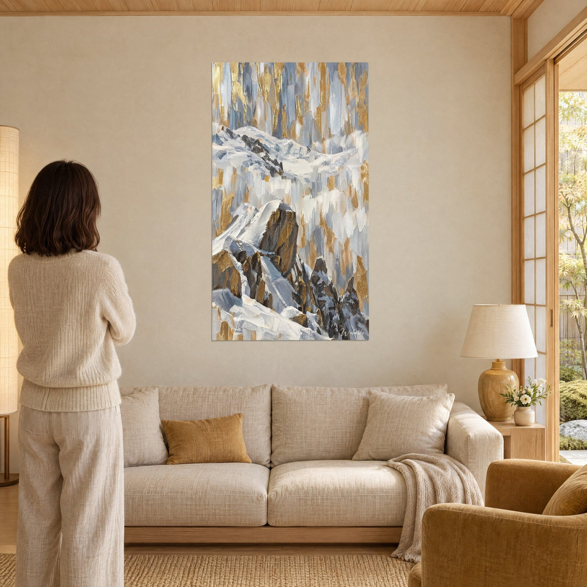 Tableau cime enneigée aux stries or et grises, femme de dos devant ses arêtes rocheuses, au-dessus d'un canapé dans un salon lumineux