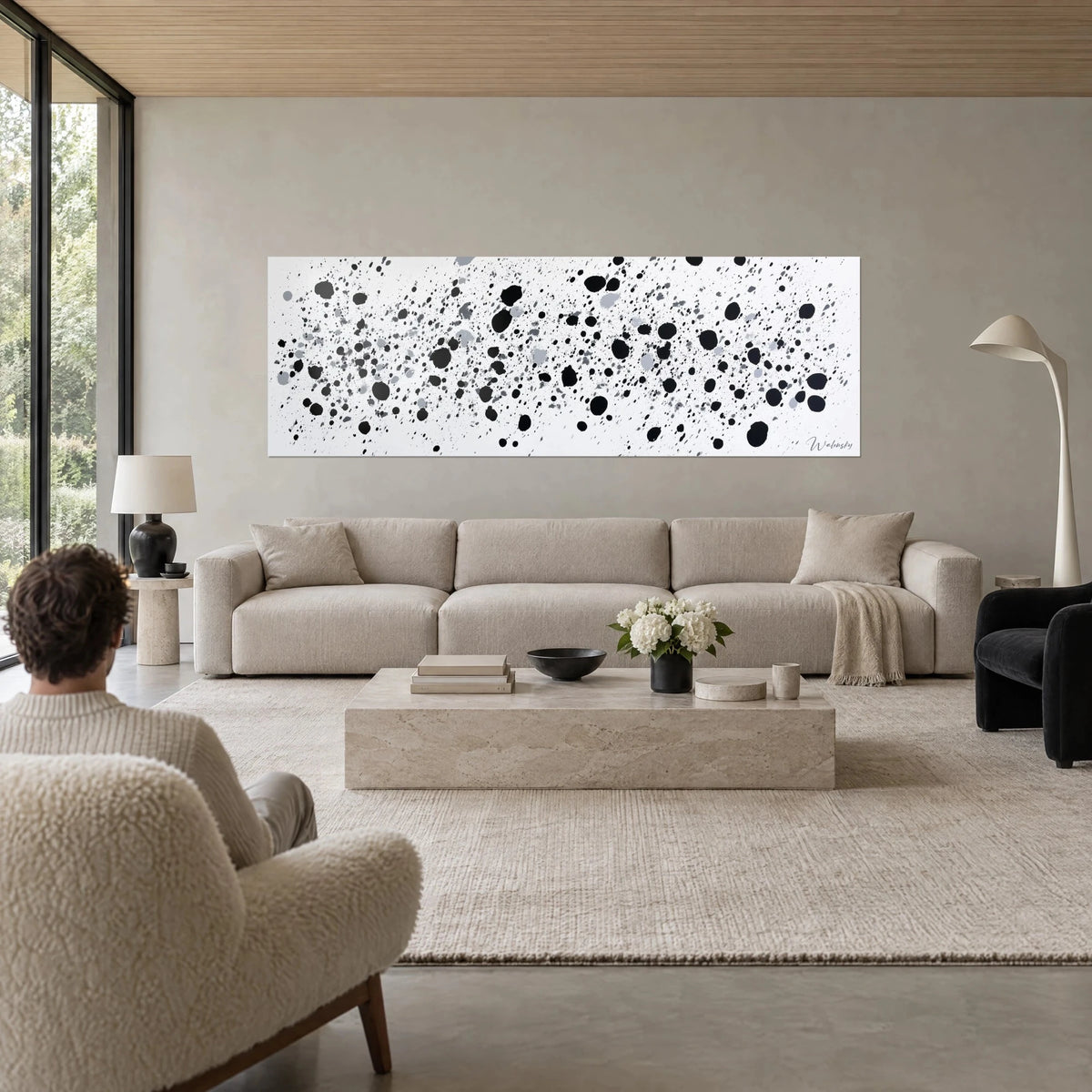 Gemälde mit schwarzen Tintentropfen, die auf weißen Hintergrund spritzen, Graustufen, eine Person von hinten, über einem Sofa in einem hellen Wohnzimmer
