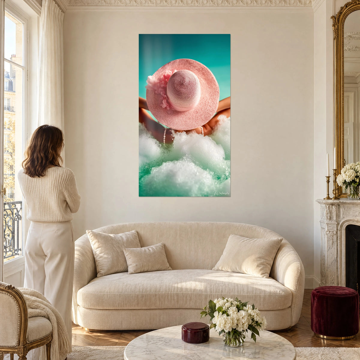 Cuadro sombrero de ala ancha rosa empolvado sobre agua turquesa y espuma blanca, mujer de espaldas, encima de un sofá en un salón luminoso