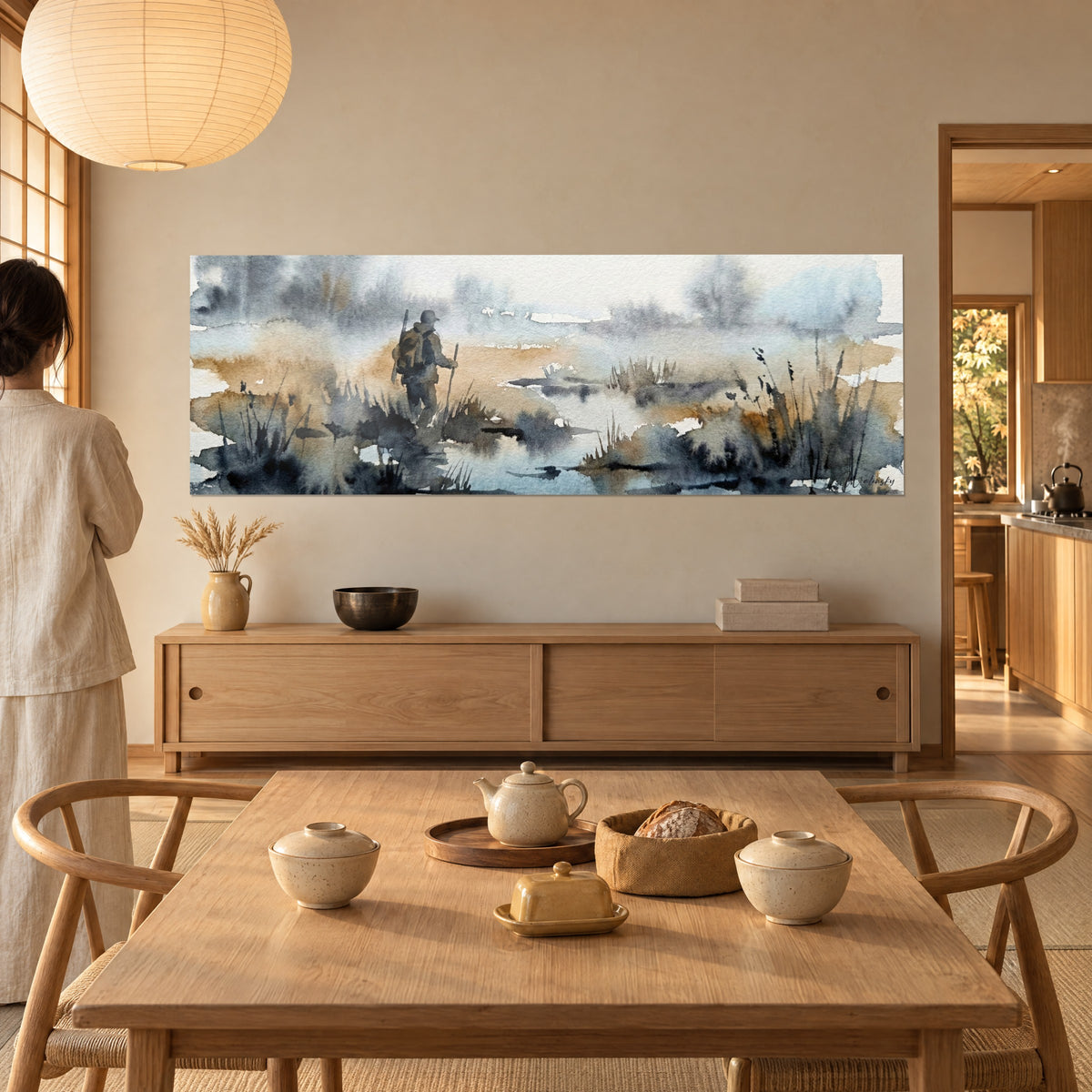 Tableau randonneur et sa canne au bord d'une eau grise, herbes sombres et sable ocre, face à une table de salle à manger en bois