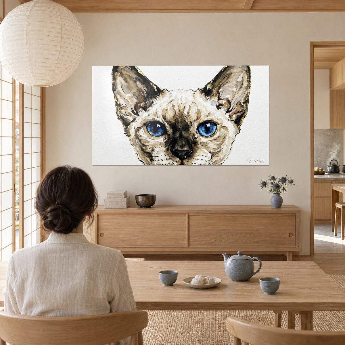 Quadro ritratto di gatto Devon rex ad acquerello, pelo sabbia e talpa, occhi azzurri luminosi, osservato da una donna di spalle in un soggiorno japandi