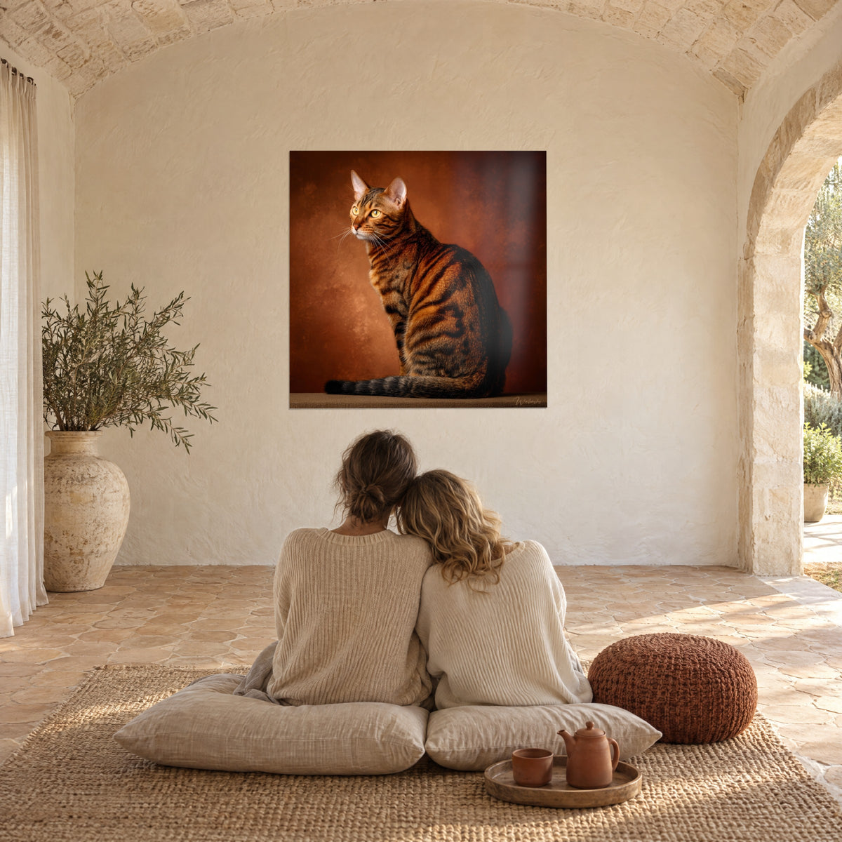 Πίνακας ξανθιάς γάτας Toyger με ρίγες από έβενο, δακτυλιωτή ουρά, φόντο τερακότα, μπροστά σε ζευγάρι καθισμένο σε μαξιλάρια