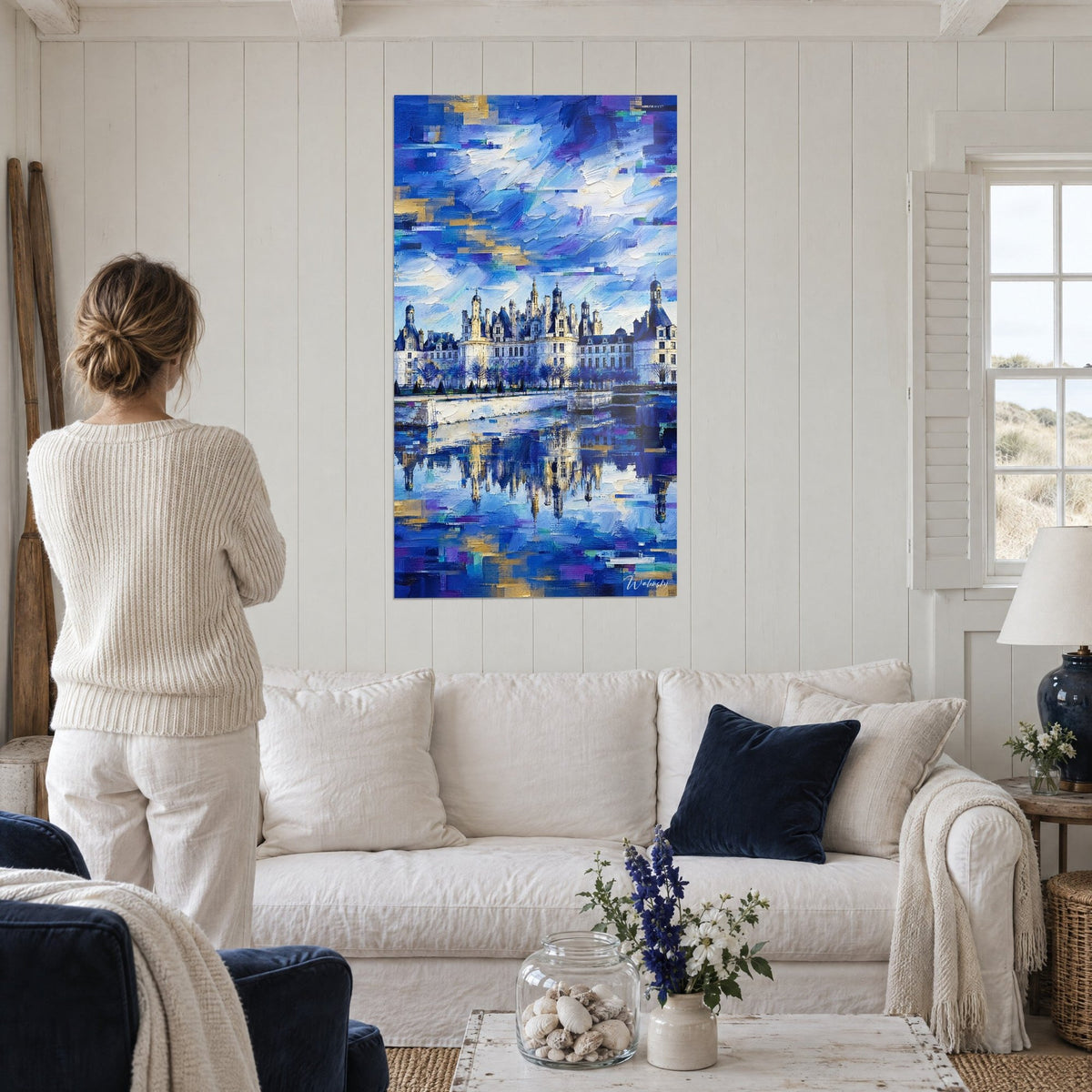 Tableau château Renaissance aux tourelles ardoise, ciel bleu cobalt et touches dorées, femme de dos au-dessus d'un canapé dans un salon lumineux