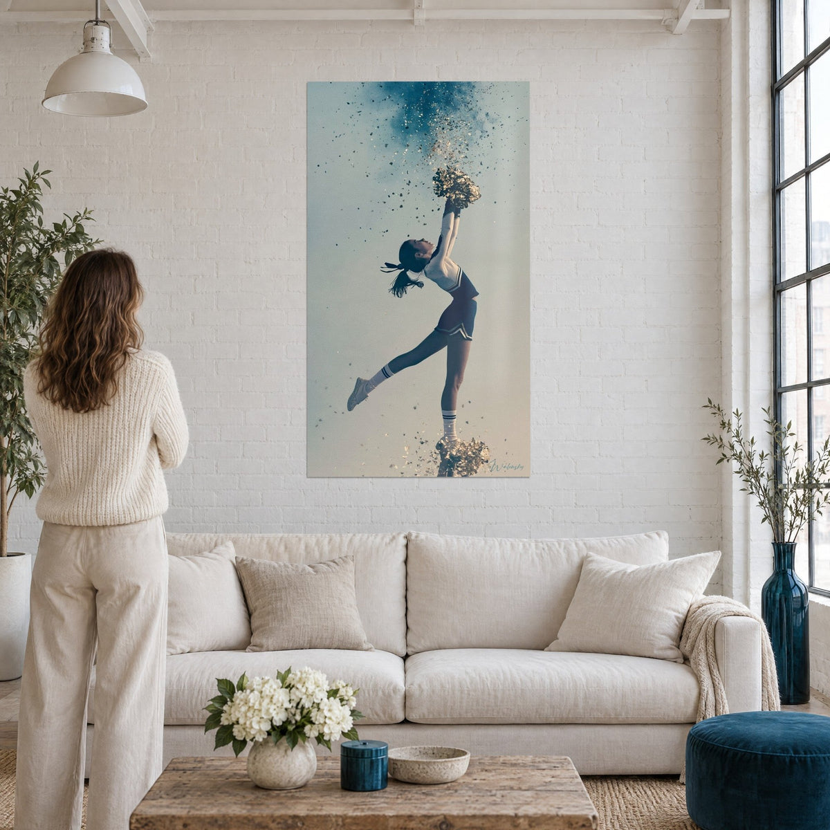 Wall art of a cheerleader arched back in navy blue and gold, cloud of glitter, above a sofa in a bright living room