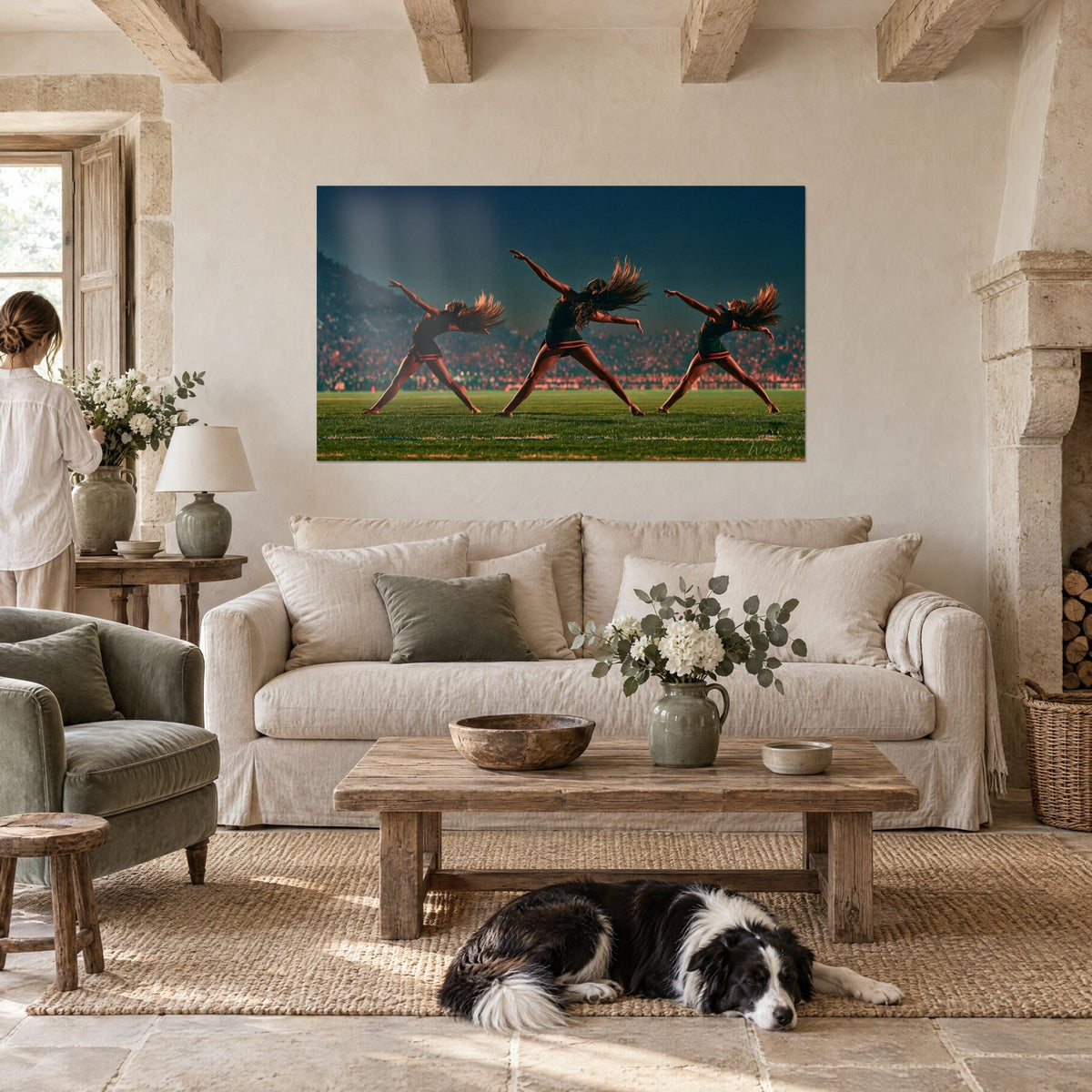 Wall art three cheerleaders in full mid-air leap, green skirts with orange trim, flowing hair, above a sofa in a bright living room
