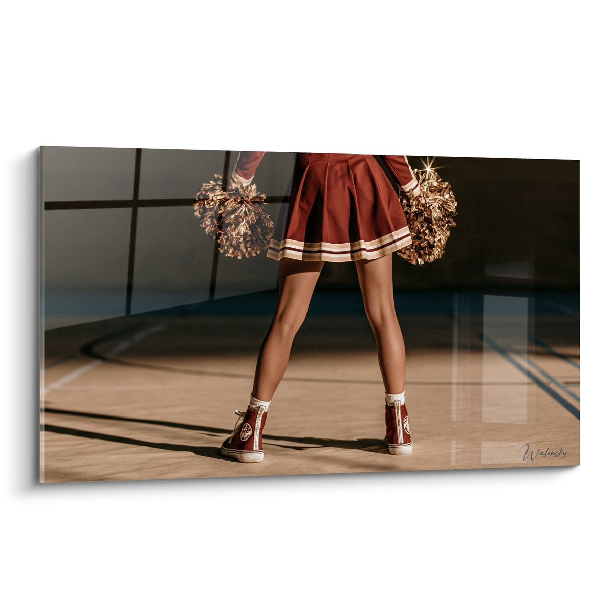 Pom-pom girl aux jambes fermes, jupe bordeaux et pompons dorés sur parquet camel