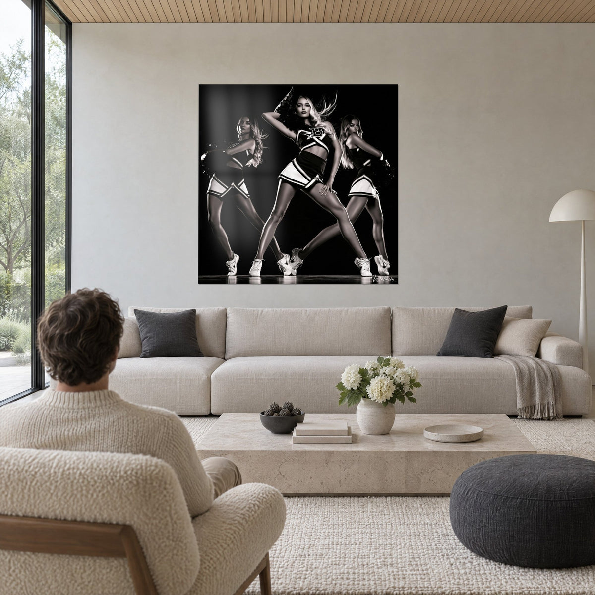 Quadro pom-pom girl bionda in posa conquistatrice, due compagne in bianco e nero, sopra un divano in un soggiorno luminoso
