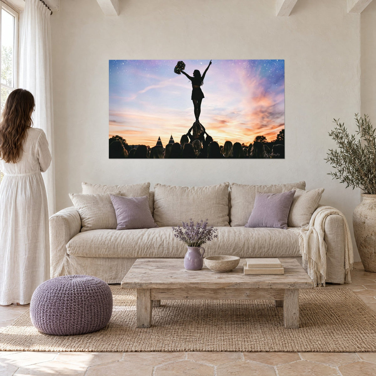 Wall art cheerleader silhouette, arm raised with golden pom-pom, orange and purple sky, above a sofa in a bright living room