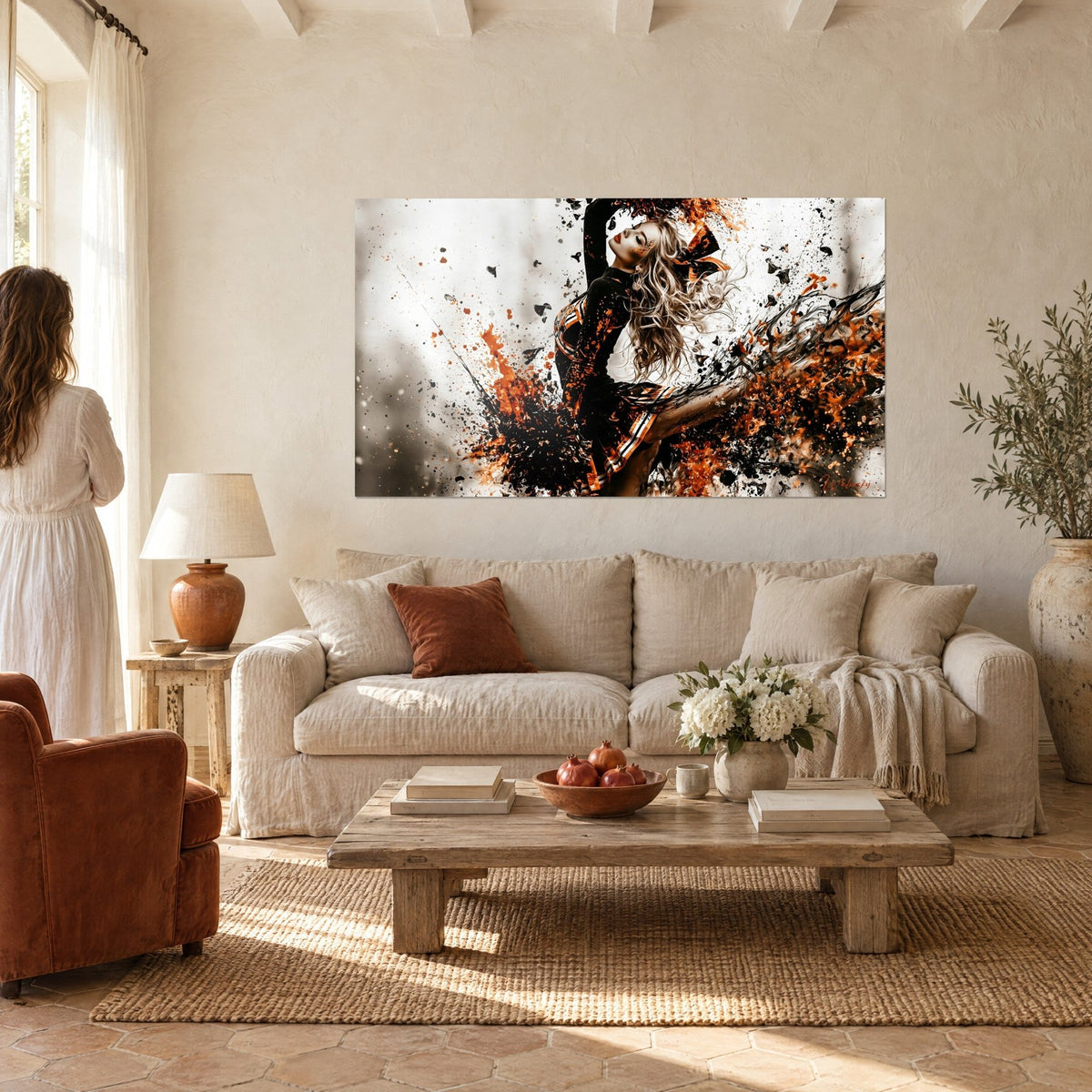 Tableau pom-pom girl blonde en pleine pirouette, éclaboussures orange et noires, au-dessus d'un canapé dans un salon lumineux