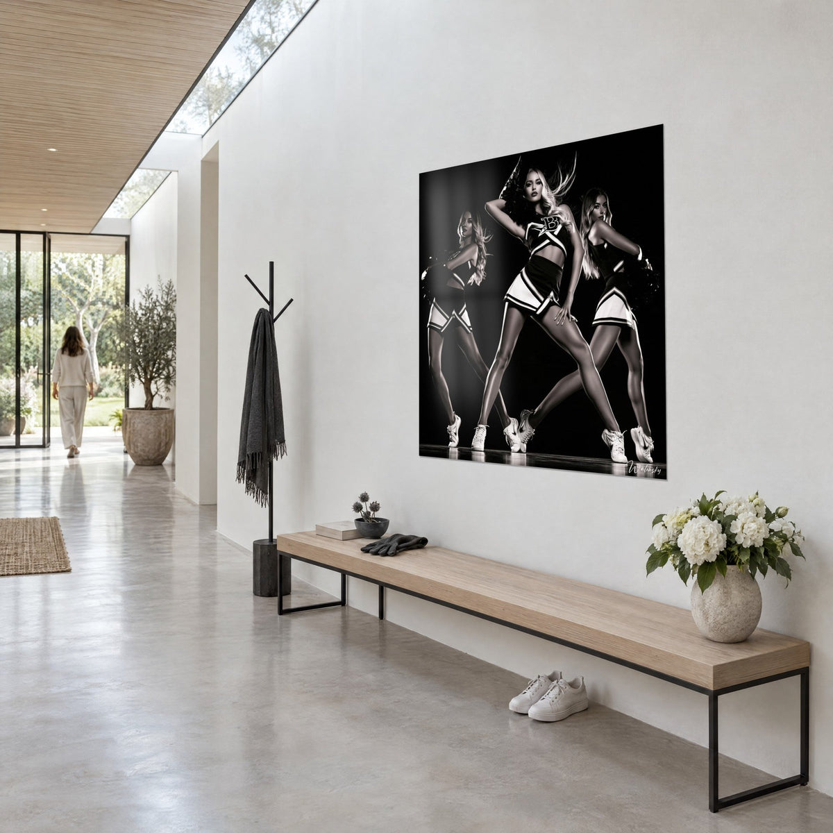 Quadro trio di pom-pom girl in divise nere e avorio, gambe divaricate su sfondo scuro, parete bianca e panca in legno
