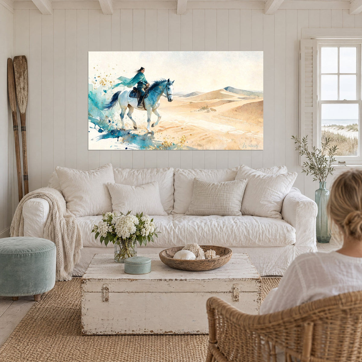 Cuadro jinete con capa turquesa sobre caballo blanco, dunas doradas en acuarela, encima de un sofá en un salón luminoso