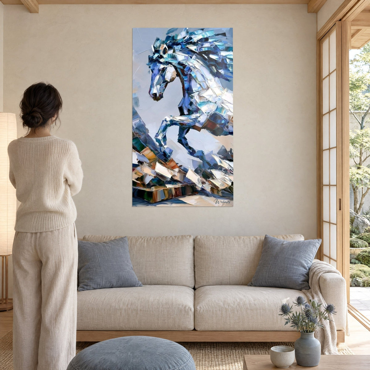 Quadro di uno stallone impennato in pennellate a spatola di blu cobalto e bianco madreperla, donna di spalle, sopra un divano in un soggiorno luminoso