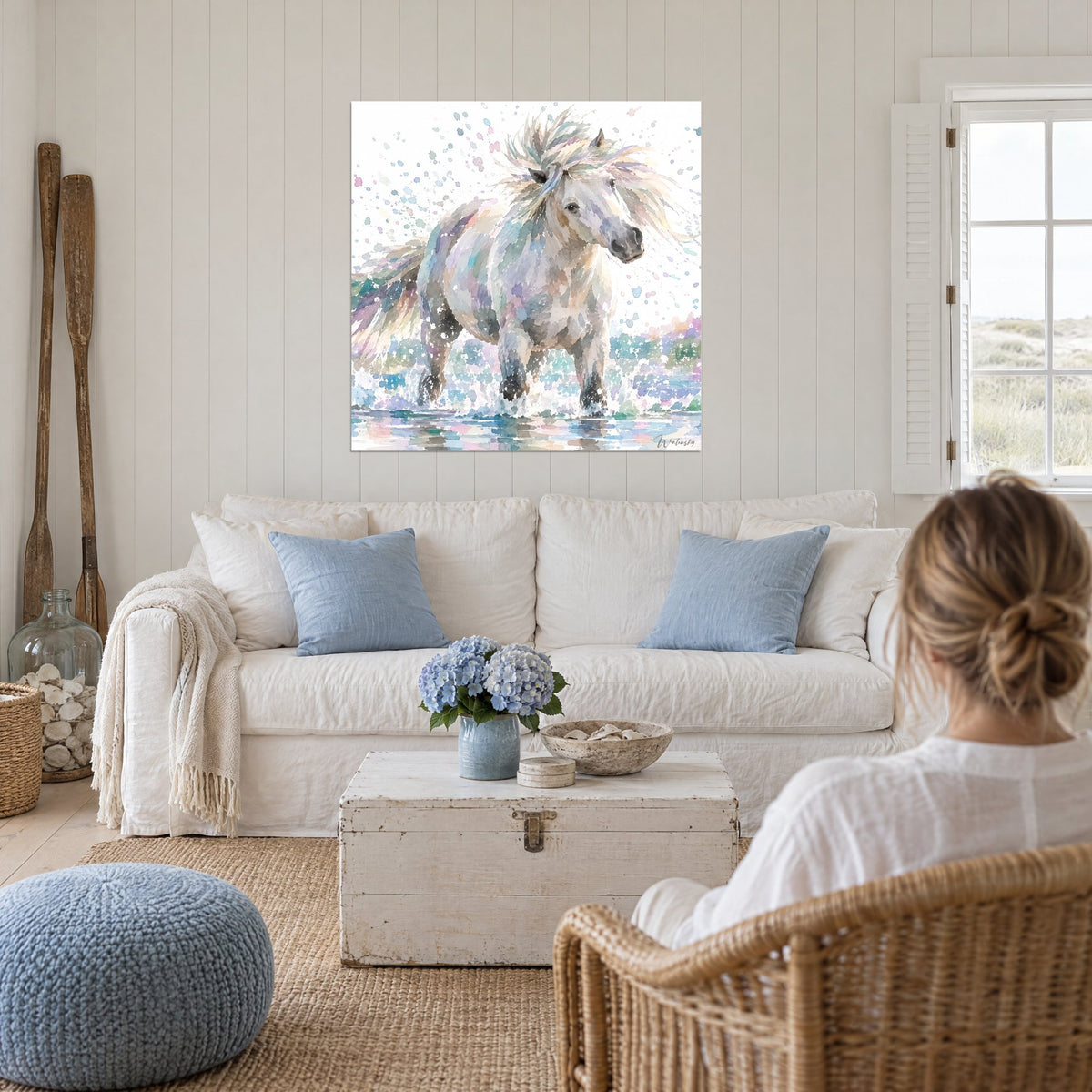 Tableau cheval blanc à la crinière lavande et pêche, éclaboussures bleues, au-dessus d'un canapé dans un salon lumineux