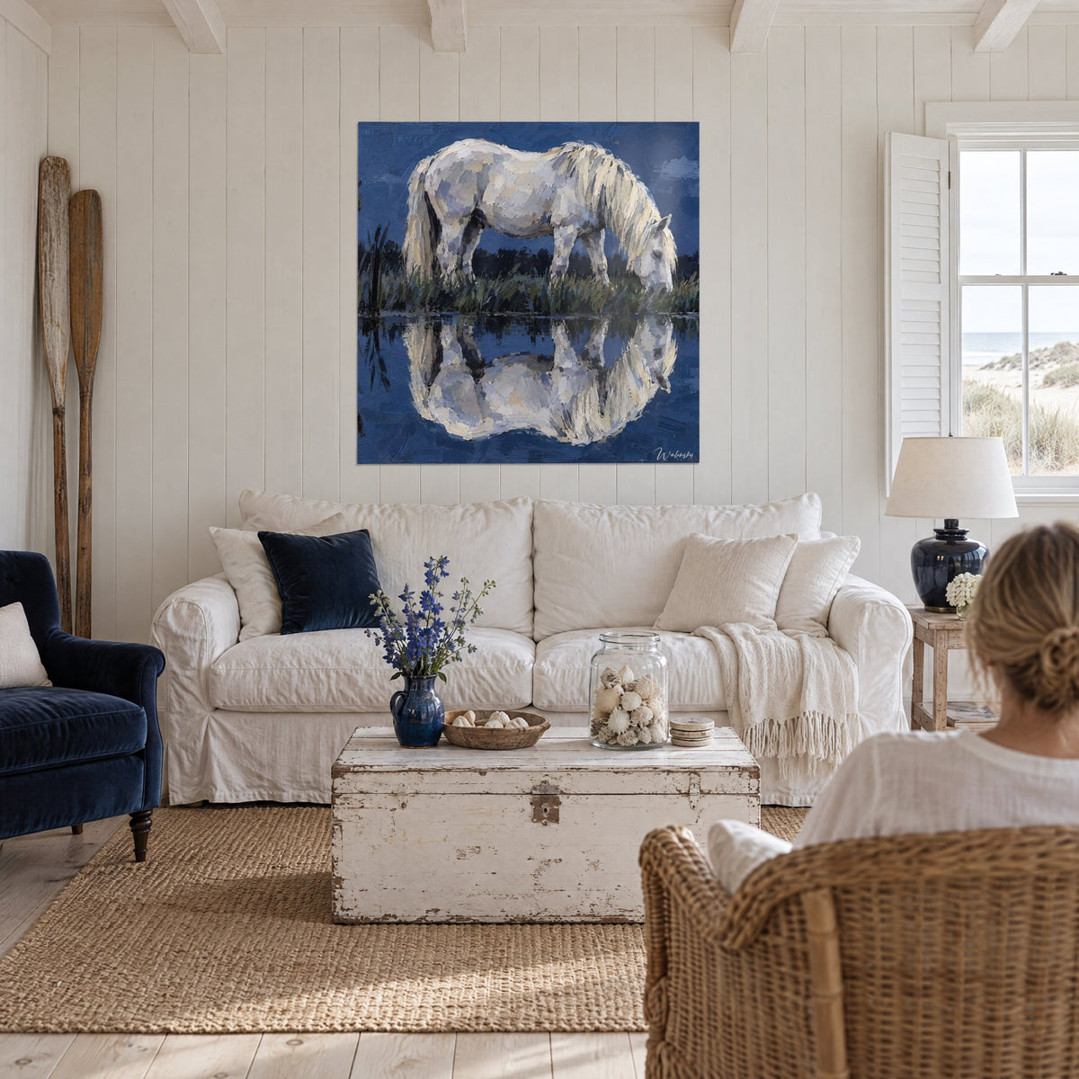 Tableau cheval blanc broutant l'herbe au bord d'un étang bleu nuit, crinière ivoire, au-dessus d'un canapé dans un salon lumineux