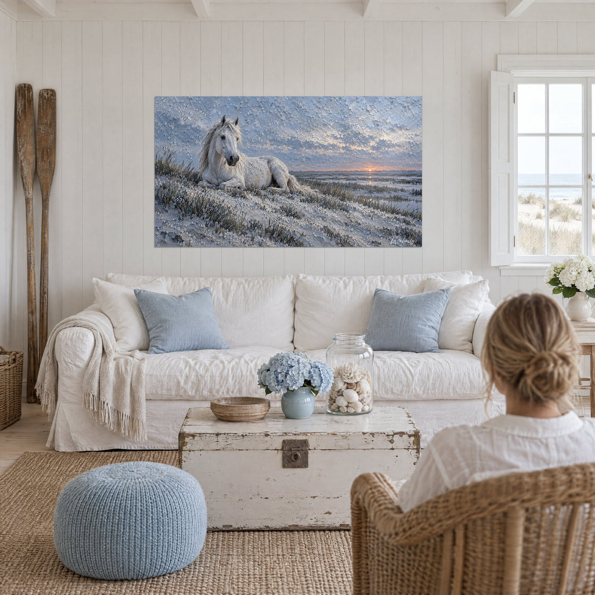 Tableau cheval blanc couché sur une dune, ciel bleu-gris et soleil orangé, au-dessus d'un canapé dans un salon lumineux