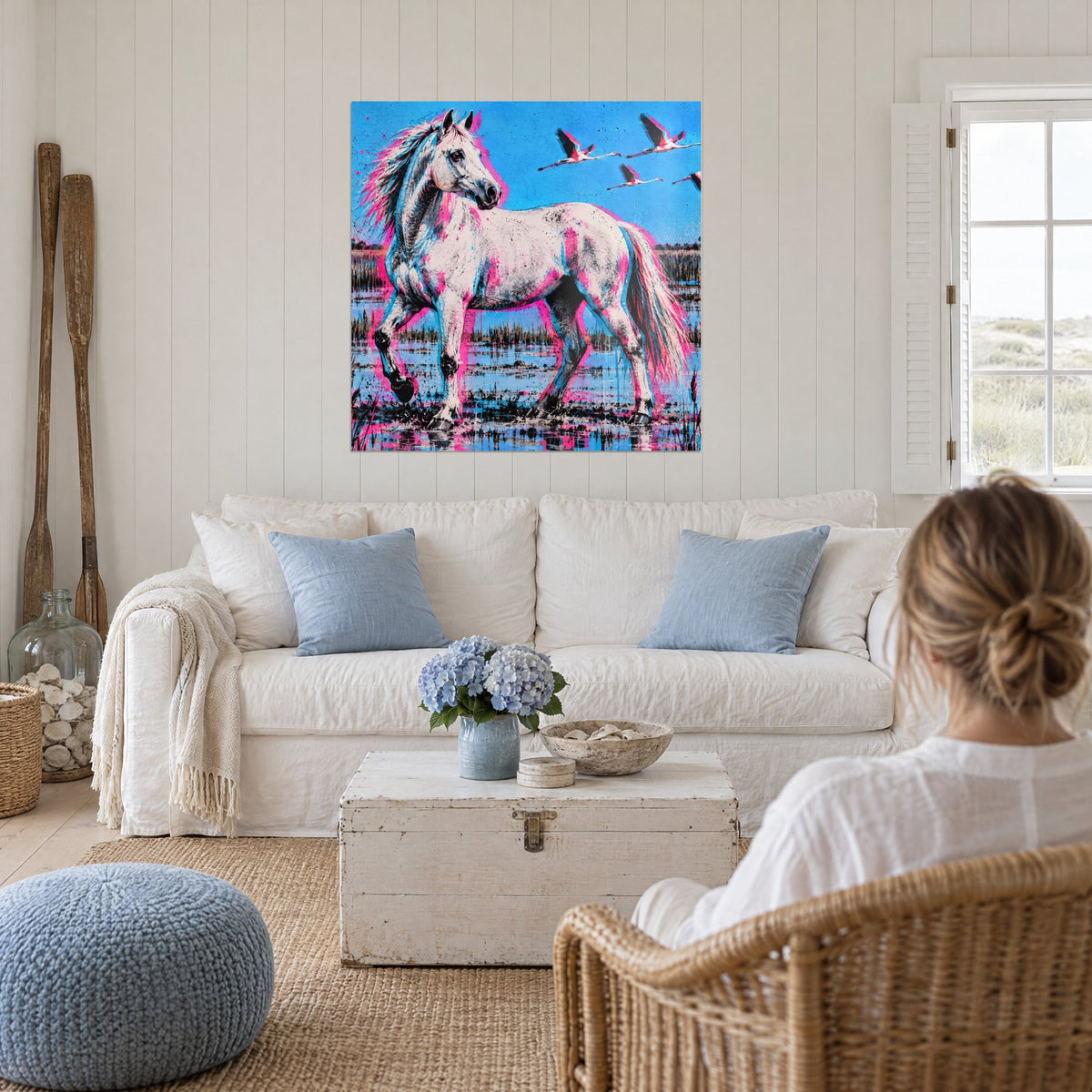 Tableau cheval blanc éclaboussé de rose et de bleu, trois flamants en vol, au-dessus d'un canapé dans un salon lumineux