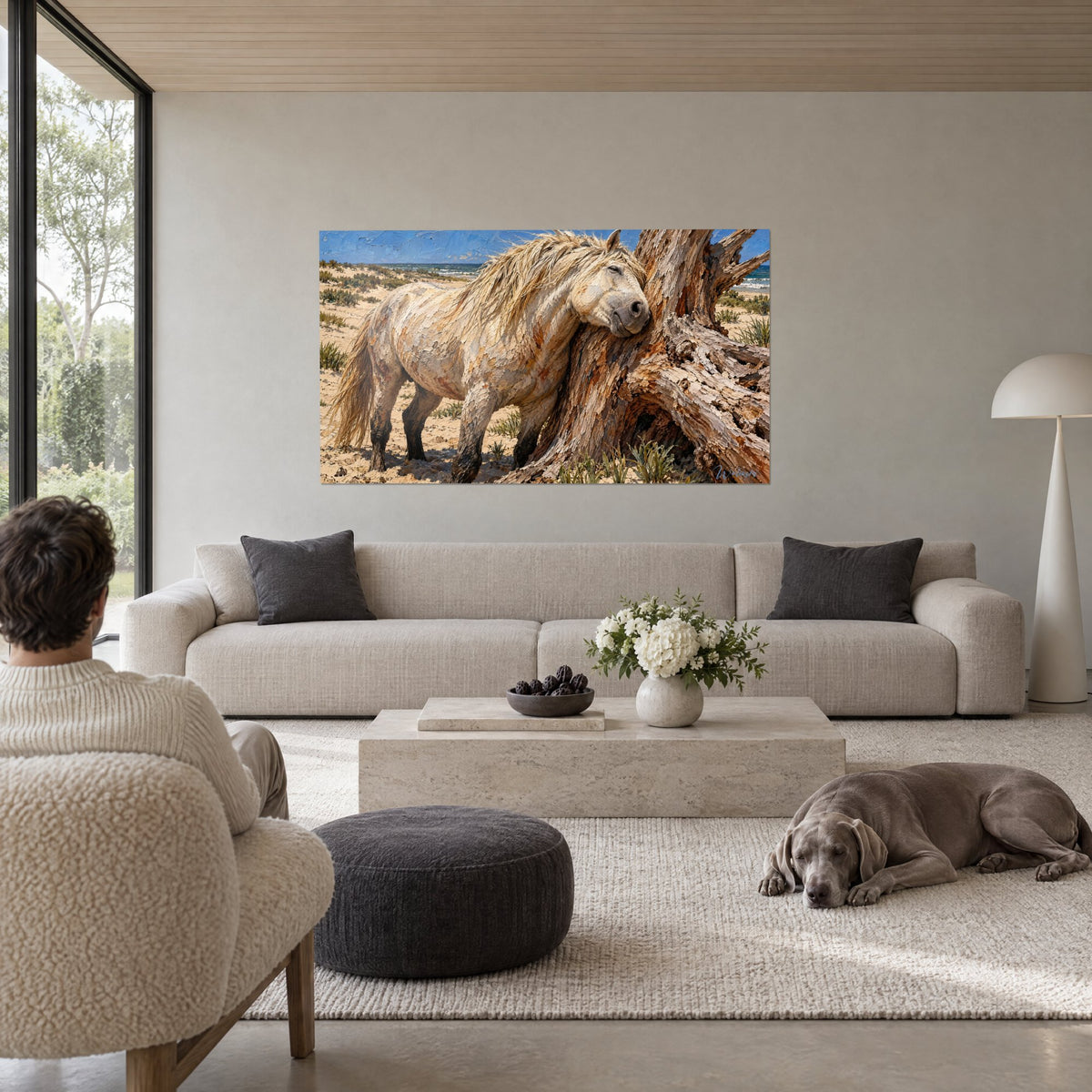 Tableau cheval camarguais crème appuyé contre un tronc brun, mer bleue au loin, au-dessus d'un canapé dans un salon lumineux