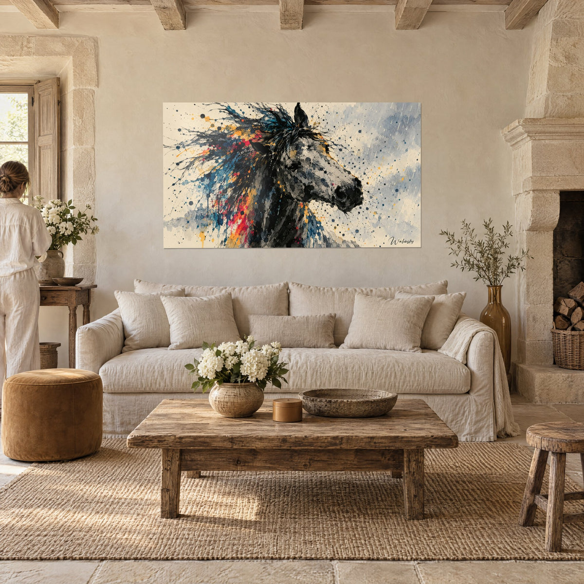 Tableau cheval gris pommelé à crinière éclaboussée de bleu et de rouge, devant une femme de dos, au-dessus d'un canapé dans un salon lumineux