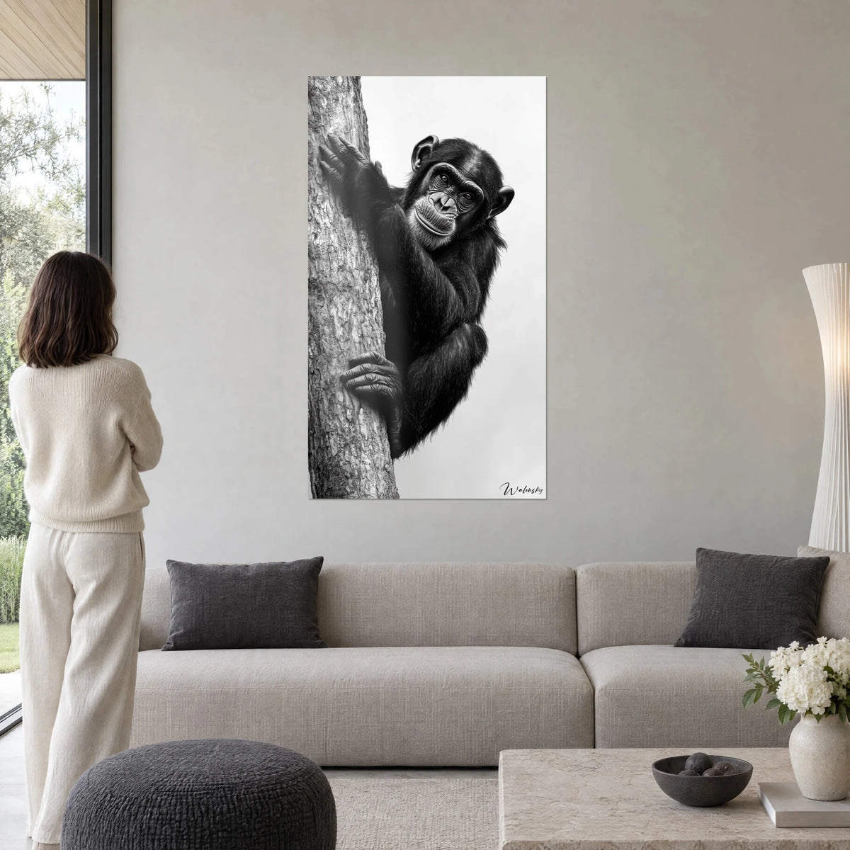 Wall art black chimpanzee clinging to the grey trunk, amber gaze on white background, woman seen from behind, above a sofa in a bright living room