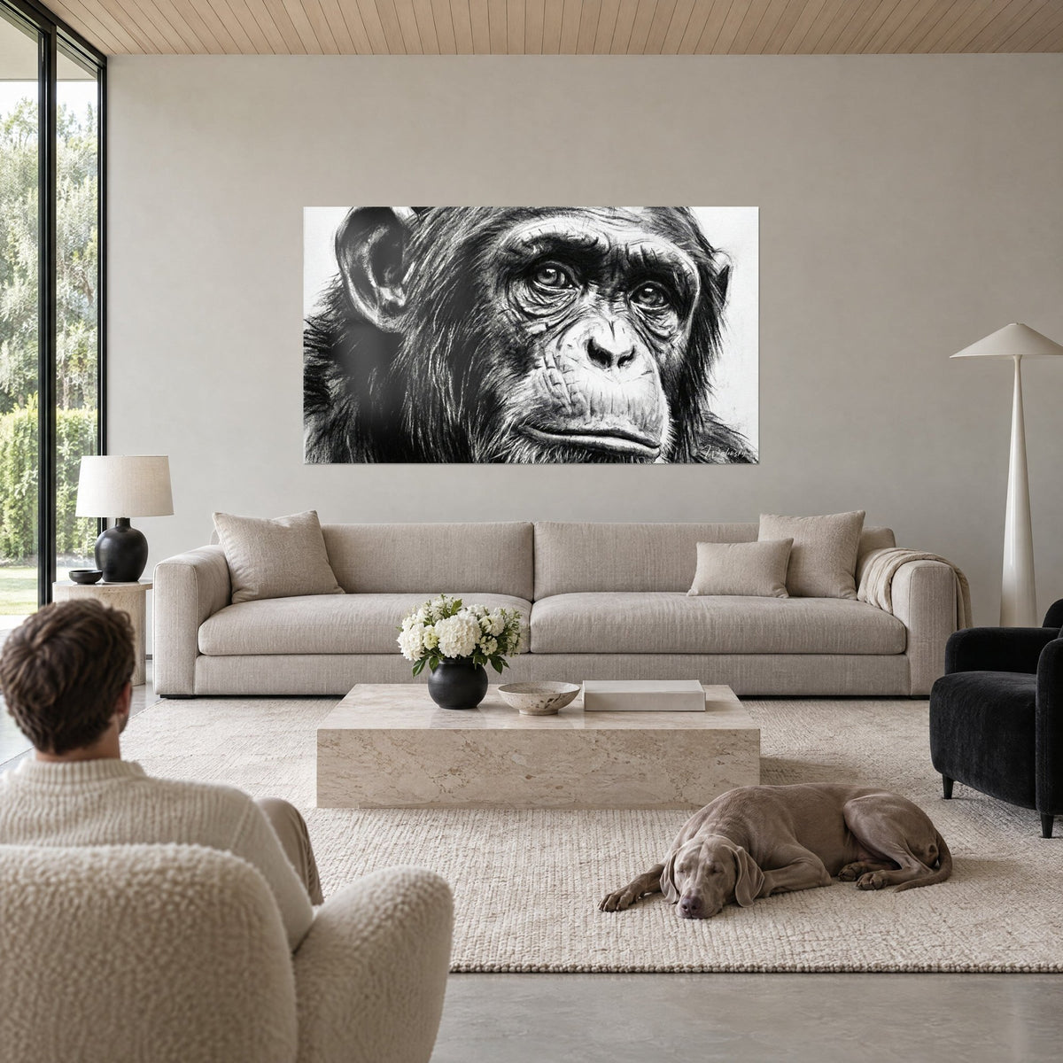 Cuadro retrato de chimpancé al carboncillo, mirada intensa en blanco y negro, dos personas de espaldas y un Weimaraner gris, encima de un sofá en un salón luminoso