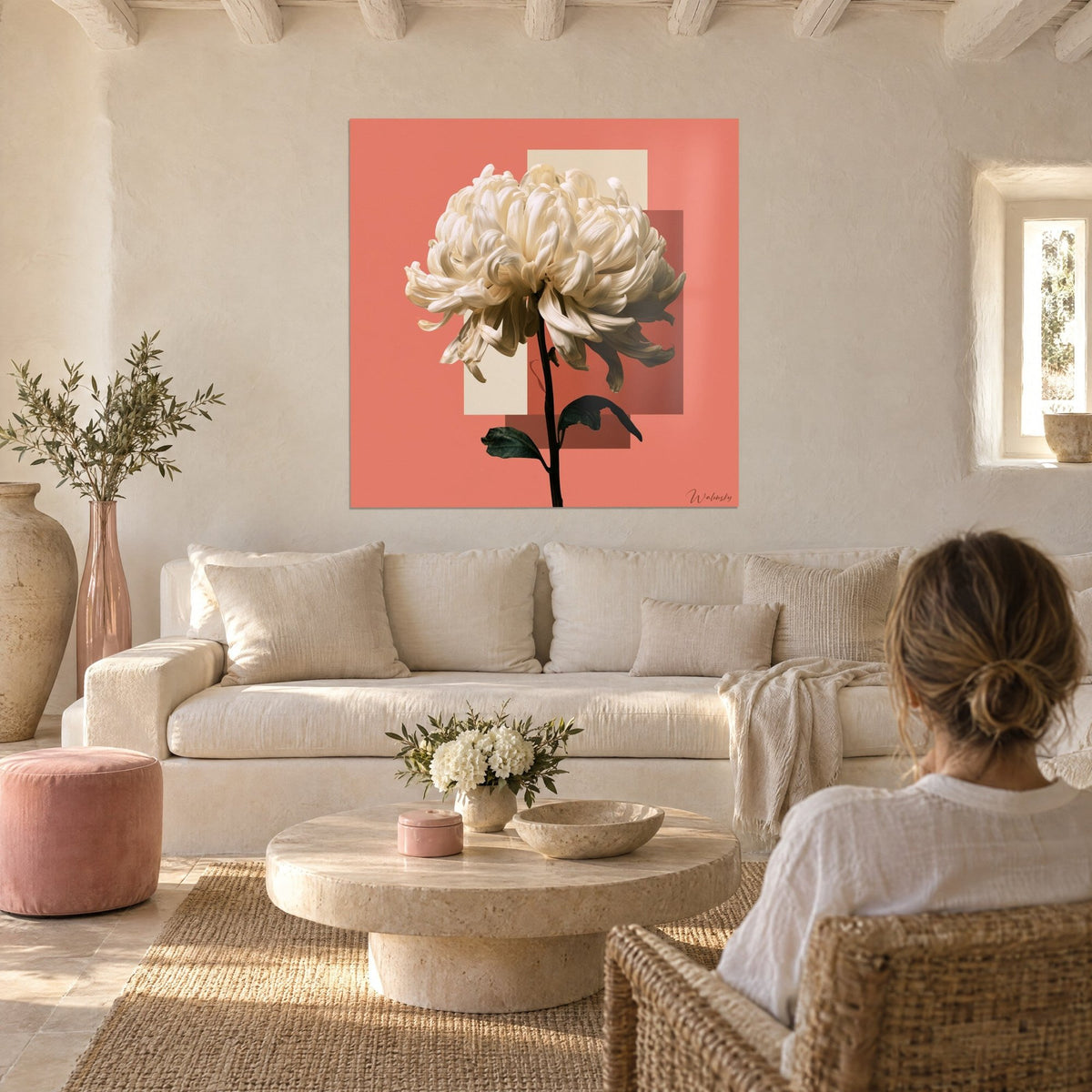 Tableau chrysanthème ivoire aux pétales ébouriffés sur fond corail et beige, femme de dos, au-dessus d'un canapé dans un salon lumineux