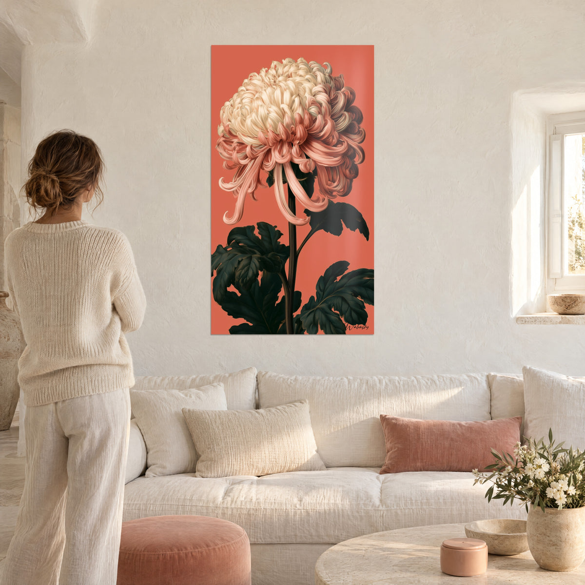 Quadro crisantemo avorio con petali ricciuti corallo su sfondo rosso arancio, donna di spalle, sopra un divano in un soggiorno luminoso