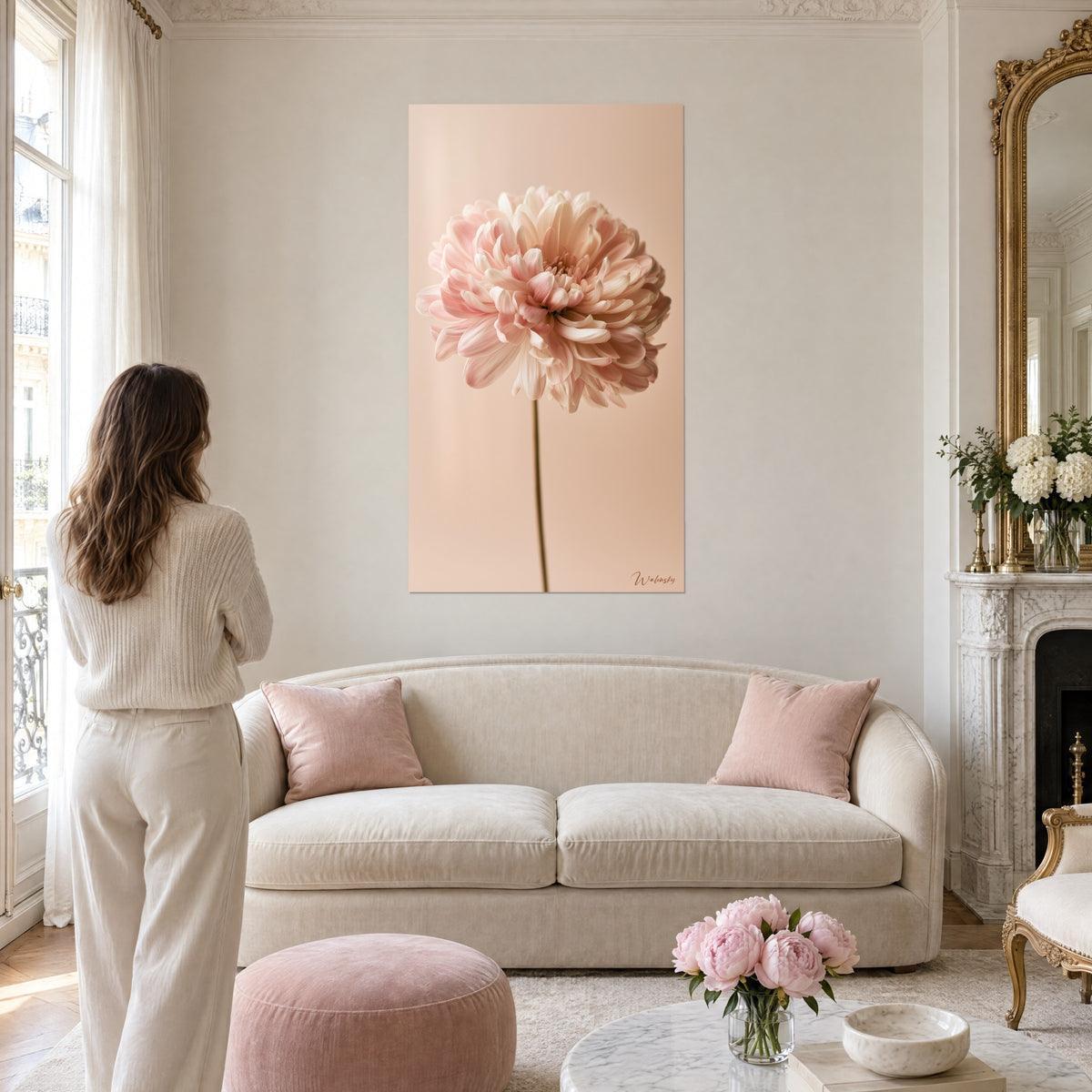 Quadro fiore di crisantemo con petali rosa cipria e crema su sfondo beige, donna di spalle, sopra un divano in un soggiorno luminoso
