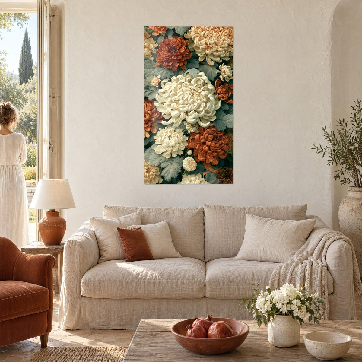 Tableau bouquet de chrysanthèmes ivoire et roux sur feuillage vert argenté, au-dessus d'un canapé dans un salon lumineux