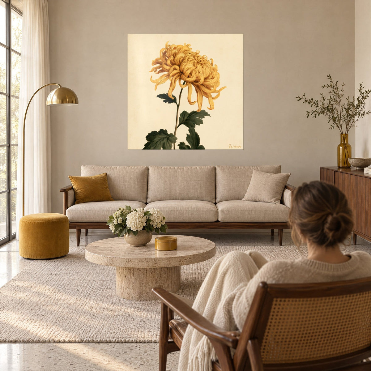 Cuadro crisantemo dorado de pétalos rizados, hojas verde oscuro sobre fondo crema, encima de un sofá en un salón luminoso