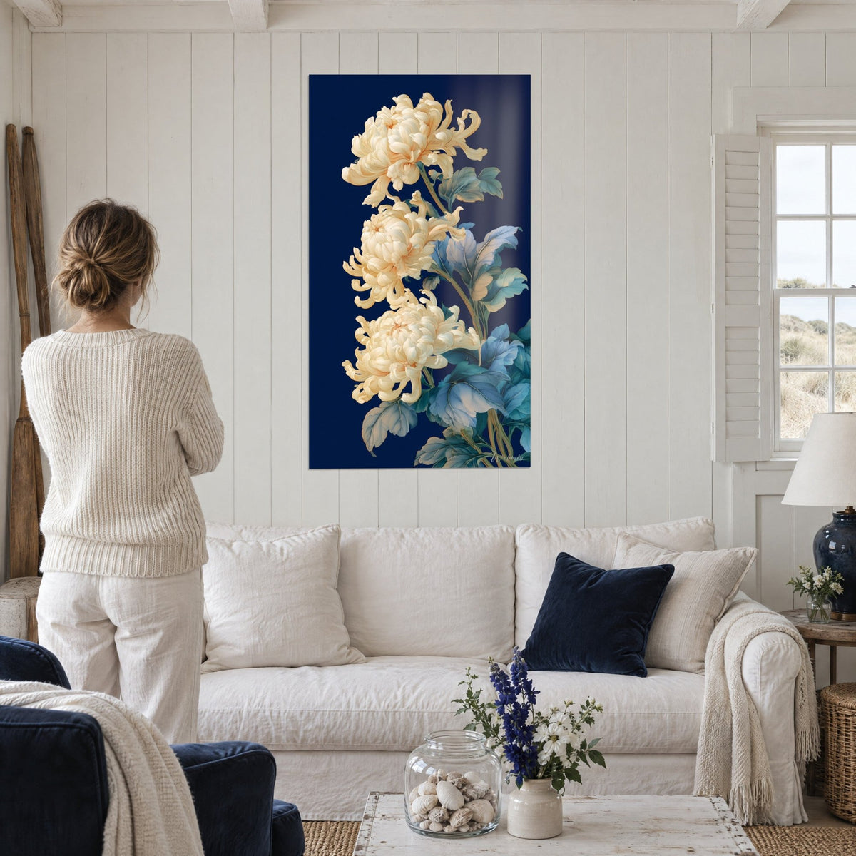 Tableau trio de chrysanthèmes ivoire sur fond bleu nuit, feuillage bleuté, au-dessus d'un canapé dans un salon lumineux