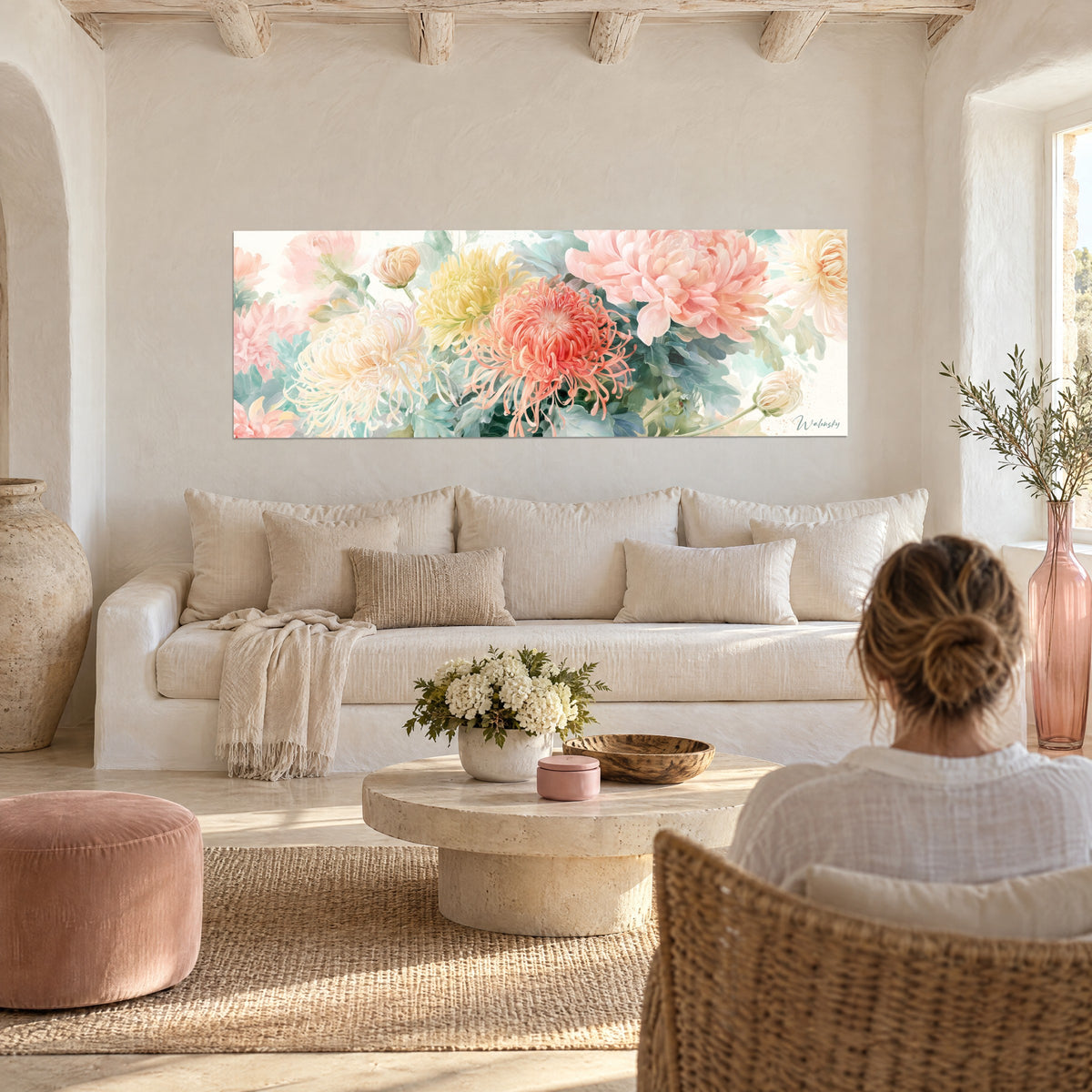 Wall art with watercolour chrysanthemums in coral and pale yellow, sea-green foliage, woman seen from behind, hanging above a sofa in a bright living room