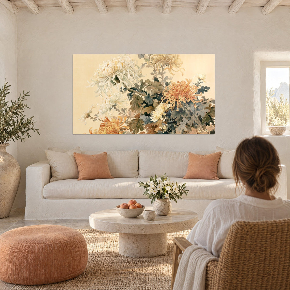 Tableau chrysanthèmes blancs et orangés en cascade sur fond crème, silhouette de dos, au-dessus d'un canapé dans un salon lumineux