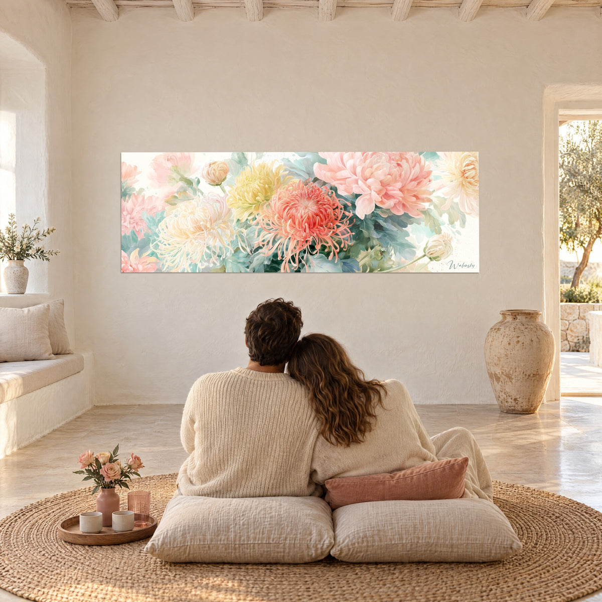 Wall art with pastel coral, yellow and powdered pink corollas, couple embracing from behind on cushions, rush mat in a whitewashed living room