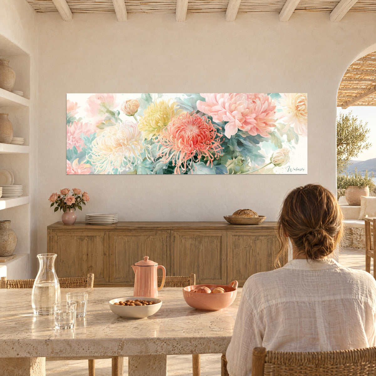 Wall art with large pastel flowers in salmon pink and butter yellow, woman seen from behind at a table, glass carafe and pink teapot in the foreground