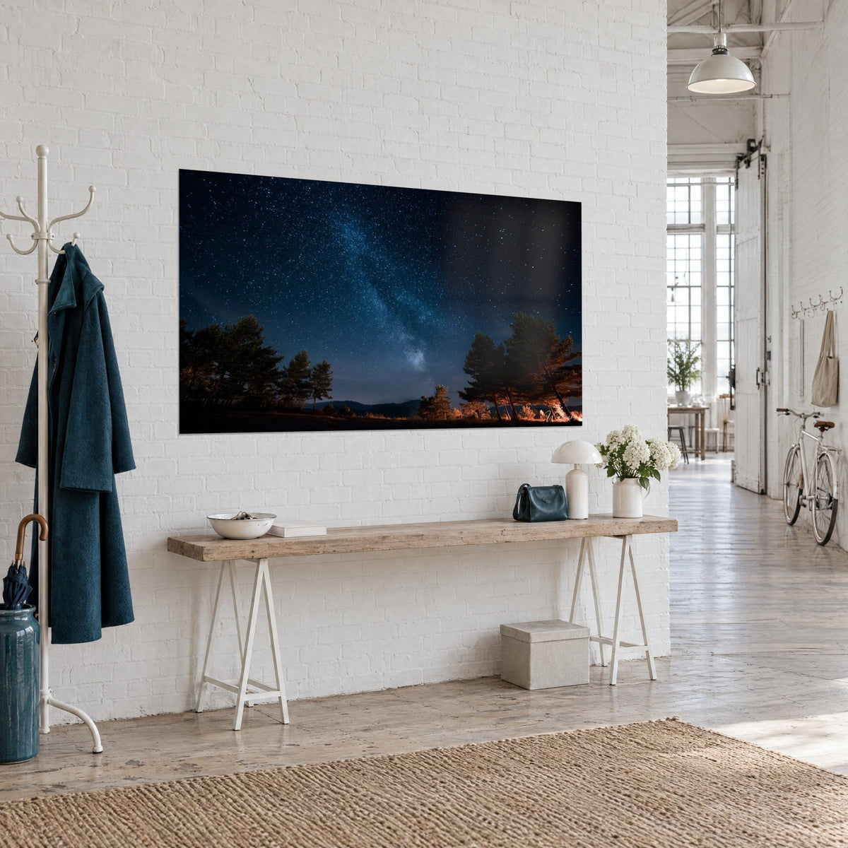 Wall art Milky Way running diagonally across an indigo sky, dark pines and amber glows, hung on the wall of a hallway in three-quarter view