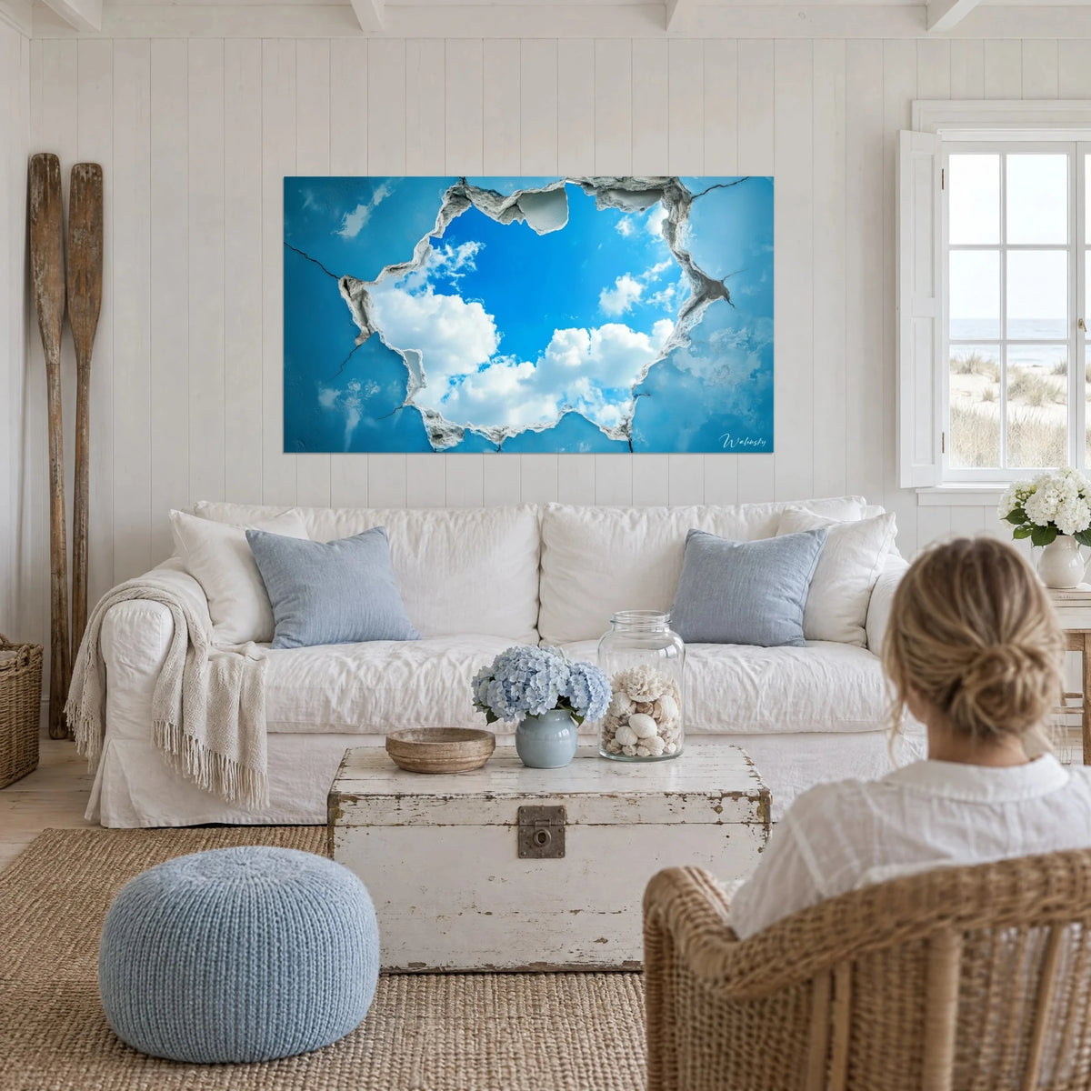 Gemälde Trompe-l'œil einer gerissenen Wand mit Durchblick auf azurblauen Himmel und weiße Wolken, über einem Sofa in einem hellen Wohnzimmer