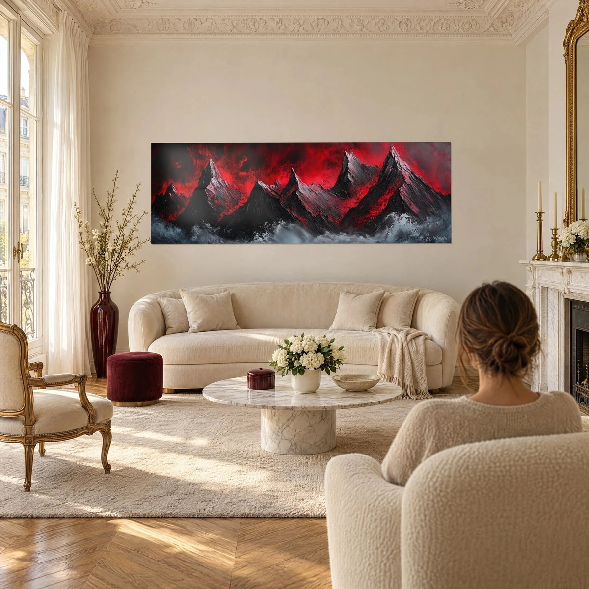 Wall art of jagged black peaks under a blood-red sky, grey foam at the bottom, woman seen from behind, above a sofa in a bright living room