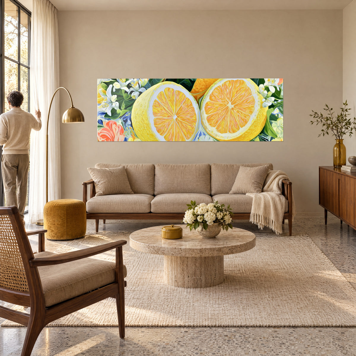 Wall art of a lemon cut in half, sunny yellow flesh and ivory rind, white blossoms, man seen from behind, above a sofa in a bright living room