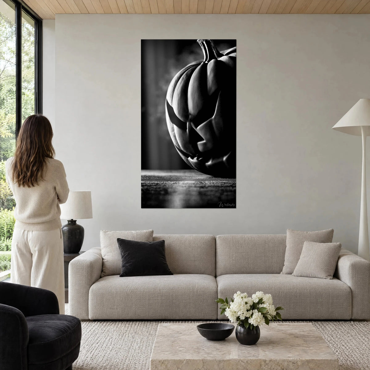 Gemälde eines grimassierenden Kürbisses in Schwarzweiß, Mandelaugen und zerrissenes Lächeln, über einem Sofa in einem hellen Wohnzimmer