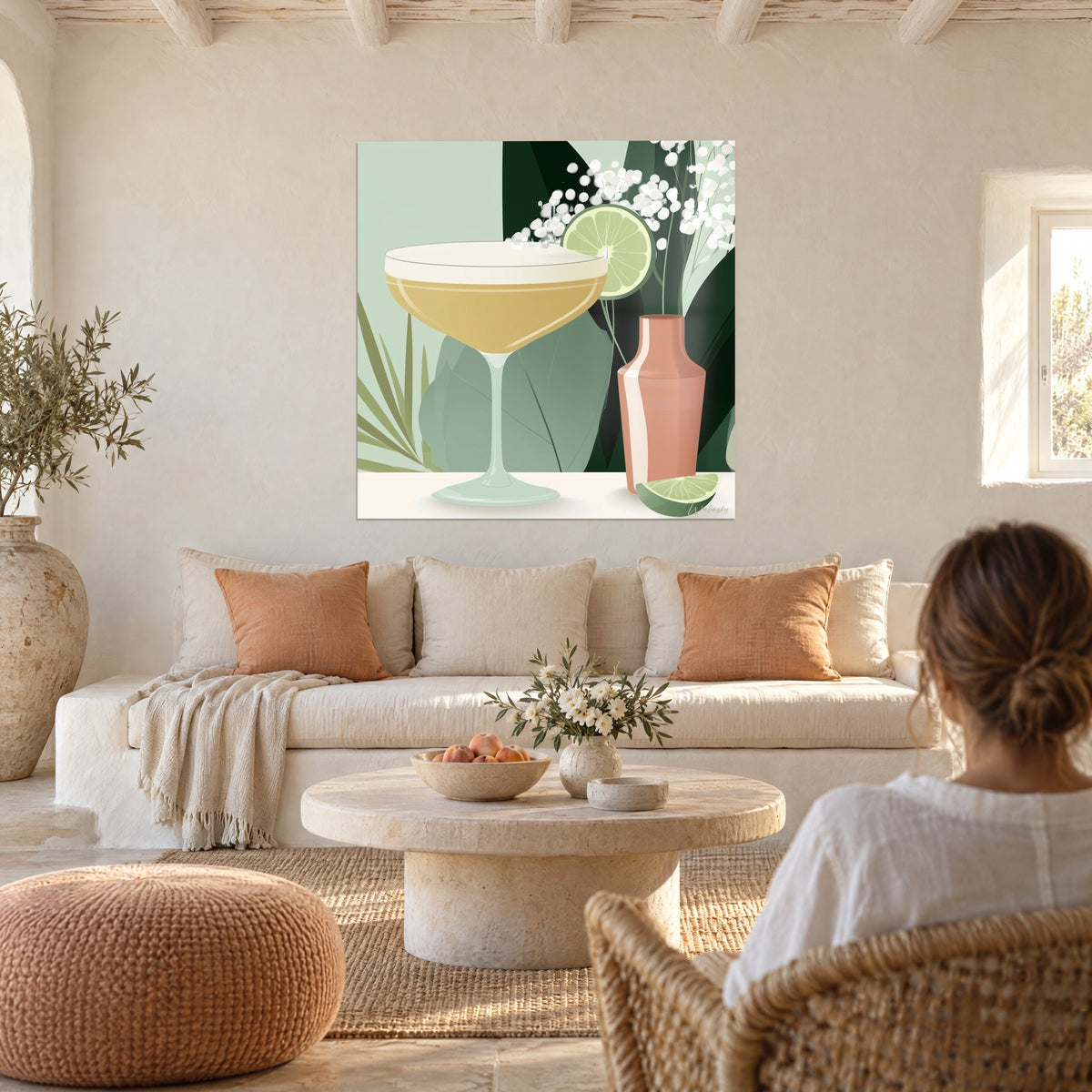 Schilderij gouden cocktailcoupe met romige schuim bovenop, limoenpartje en koraalkleurige shaker, een vrouw van achteren boven een bank in een lichte woonkamer