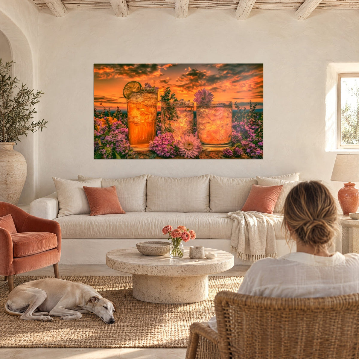 Gemälde mit drei gefrosteten Bernsteingläsern vor orangefarbenem Himmel und lila Blüten, zwei Personen von hinten, über einem Sofa in einem hellen Wohnzimmer