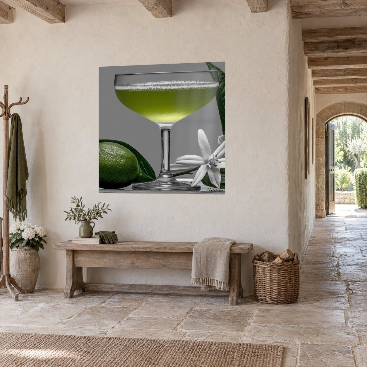 Tableau coupe à pied remplie d'un liquide vert acide, citron vert bosselé et fleur blanche, accroché dans un couloir en pierre de la maison